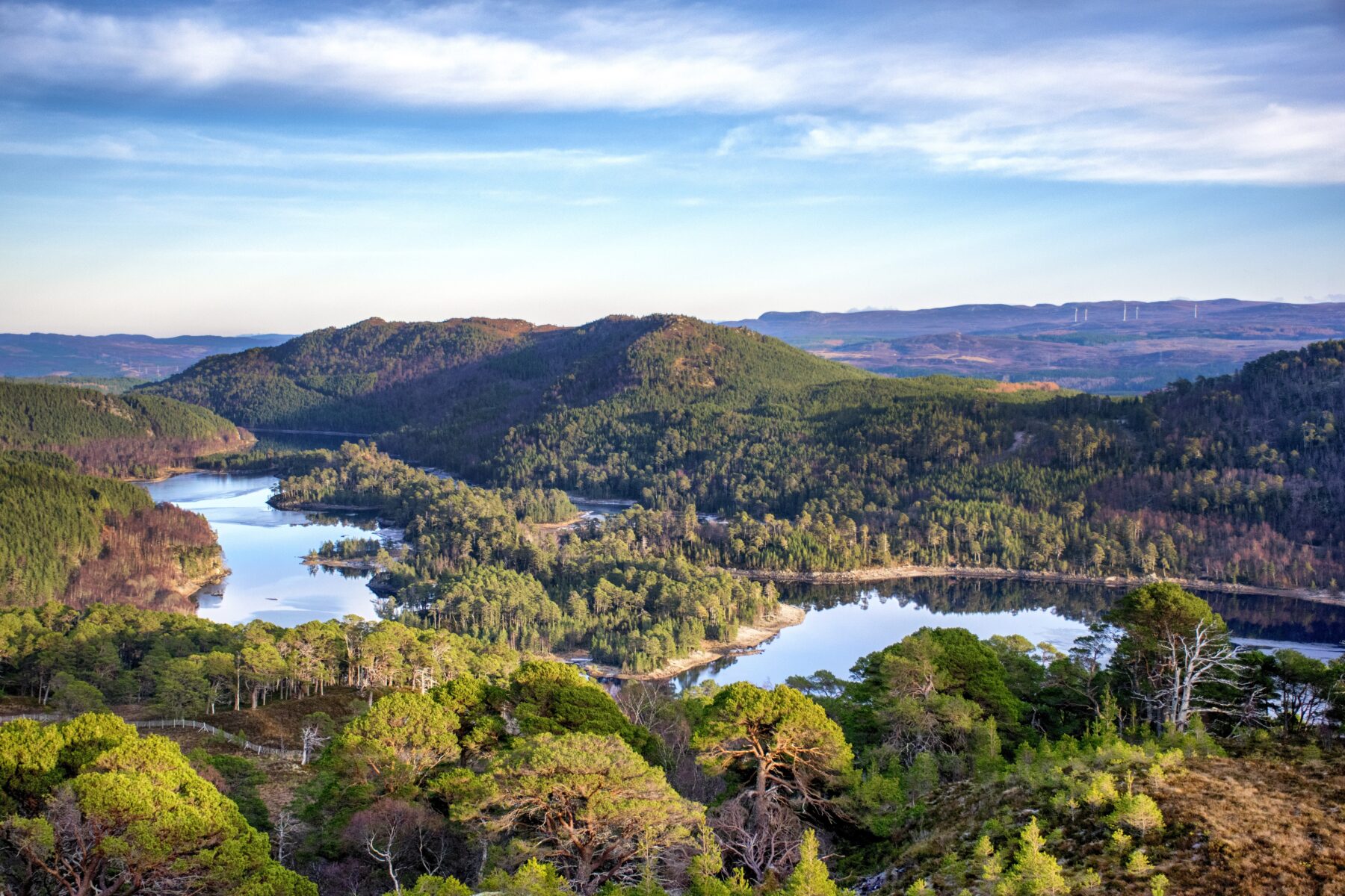 An overhead view of a green and mountainous landscape with a valley and water
