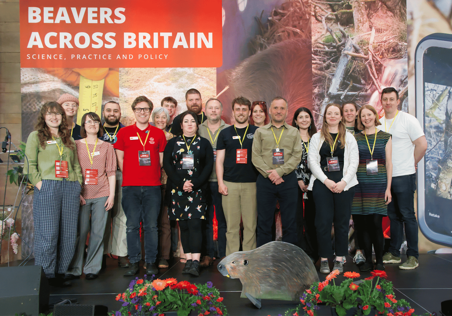 Eighteen people stood on stage in front of a large 'Beavers Across Britain" banner